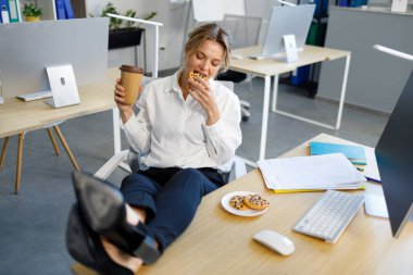 İş kadını iş yerinde kahve molası sırasında kurabiye yiyor.