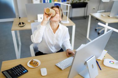 Olgun beyaz iş kadını bilgisayarda çalışıyor ve kahve içiyor.
