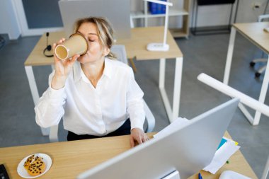 Olgun iş kadını sekreteri masasında otururken kahve içiyor.