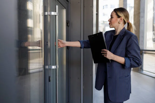 Pretty female office worker opens the door to the office building