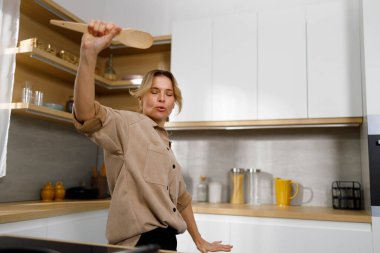 Mutfakta ahşap spatulayla dans eden komik kadın.