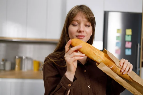 Woman sniffing a freshly baked french baguette while standing in the kitchen