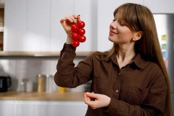 Mooie Jonge Vrouw Kijken Naar Cherry Tomaten Tak Home Keuken — Stockfoto