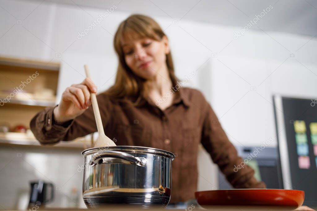 Young woman stirring something in a saucepan with a wooden spoon. Girls cooking dinner