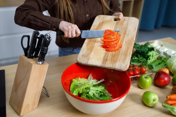 Girl in kitchen preparing fresh salad slicing vegetables throwing red paprika into bowl