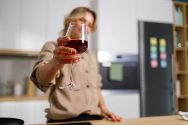 Mutfakta bir kadeh kırmızı şarap içerken tost yapan yalnız bir kadının seçici odak noktası. Olgun bir kadın bir şey kutluyor.