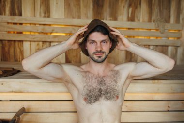 Çekici adam ahşap saunada oturup rahatlıyor.