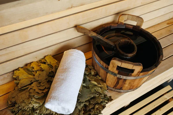 Wooden bucket with ladle, towel and broom on bench in sauna