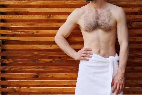 Havlu içinde kaslı vücudu olan bir adam ahşap bir duvarın arka planında poz verir.