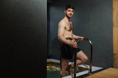 Kaslı adam spa binasındaki havuza iniyor.