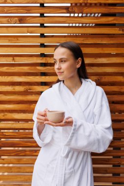 Spa otelinin terasında elinde çay olan bornozlu bir kız.