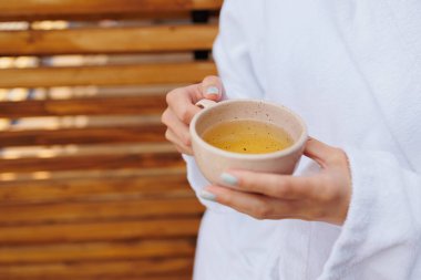 Elinde bir fincan çay tutan bornozlu bir kadın.