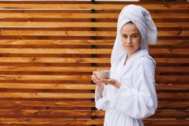 Kafası havluya sarılı bornozlu bir kadın spa otelinin terasında çay içiyor.