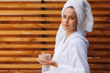 Kafasına havluyla sarılmış bornoz giymiş bir kadın güzel bir spa merkezinde çay içiyor.