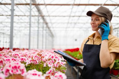 Çiçekli bir seranın güzel kadın satıcısı telefonda bir müşteriyle konuşuyor.
