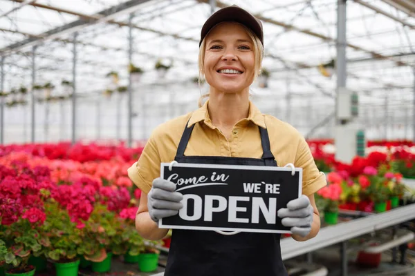 Female florist with sign we are open in greenhouse