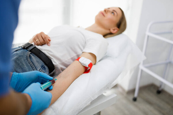 Медсестра берет кровь из вены у пациентки, лежащей на диване