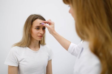 Neurologist doctor makes skin reflex test with special brush on a woman's face skin during medical appointment in clinic