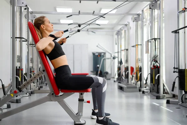 Young fitness woman training on pull cable exercising machine in gym of rehabilitation clinic