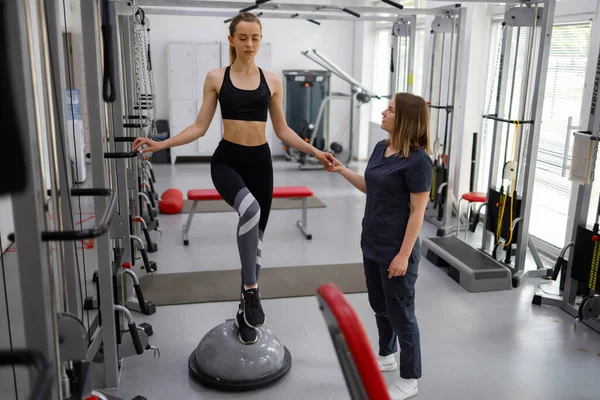 Physiotherapist helping female patient with rehabilitation. Balance exercise with bosu ball. Woman and doctor during rehab physiotherapy in gym