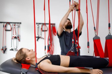 Physiotherapist assists female patient undergoing rehabilitative physiotherapy on a suspension rope system. Modern clinic using advanced rehabilitating therapy
