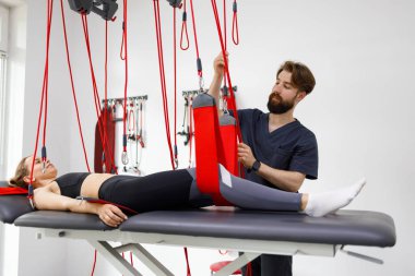 Physiotherapist doctor preparing a female patient for a neuromuscular activation procedure on a suspension rehabilitation system in a modern clinic