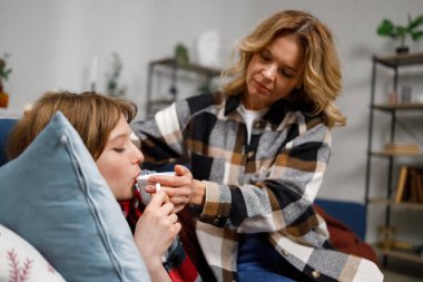 Kanepeye uzanmış ona çay veren hasta yetişkin kızına bakan olgun bir anne.