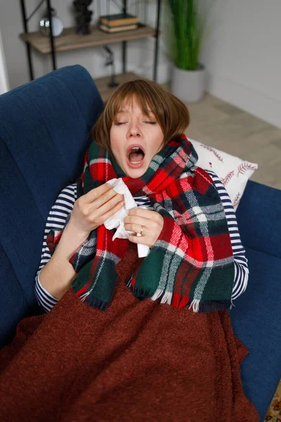 Cold woman lying on the sofa at home sneezes into a paper handkerchief