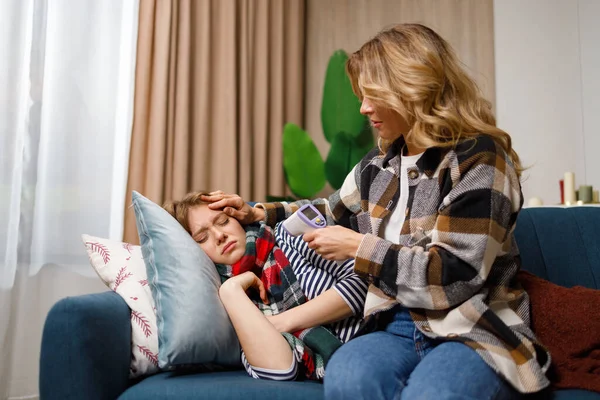 Woman with infrared thermometer measures the temperature of her daughter who is sick with the flu