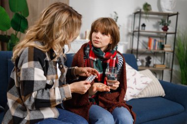 Anne kızına grip ilacı veriyor. Hasta bir kıza bakan bir kadın.