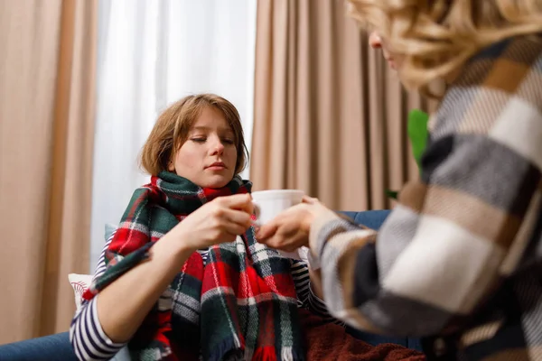 Mother gives a mug of hot tea to her daughter who is sick with the flu