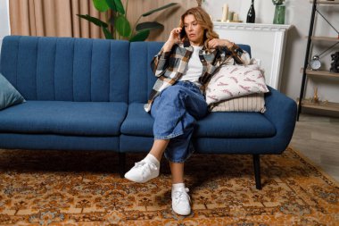 Evde kanepede otururken telefonda konuşan çekici, olgun bir kadın.