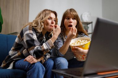 Farklı yaşlarda, kanepede patlamış mısırlı iki kadın boş zamanlarını dizüstü bilgisayarlarında film izleyerek geçiriyorlar.
