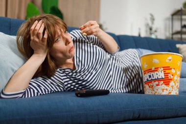 Depresyondaki genç bir kadın kanepede uzanıp patlamış mısır yiyor ve erkek arkadaşından ayrıldıktan sonra TV seyrediyor ya da yoğun bir iş gününden sonra.