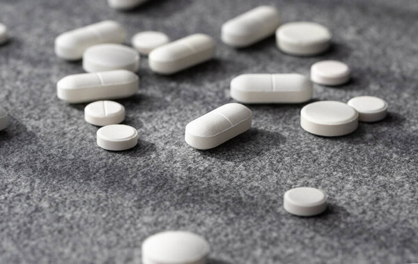 close-up white pill on gray background among others. Scattered medicines on the table