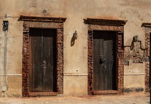 Ruined facade with two old wooden doors and dirty street lamp