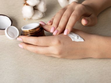 Kadının elindeki beyaz besleyici krem. Kız eline krem sürüyor ve kremin dokusunu kontrol ediyor.