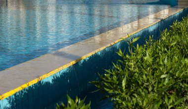 Yüzme havuzunun kenarına odaklanmış bir çerçeve ve suyun mavi yüzeyi. Temiz su havuzun kenarlarından aşağı akıyor.