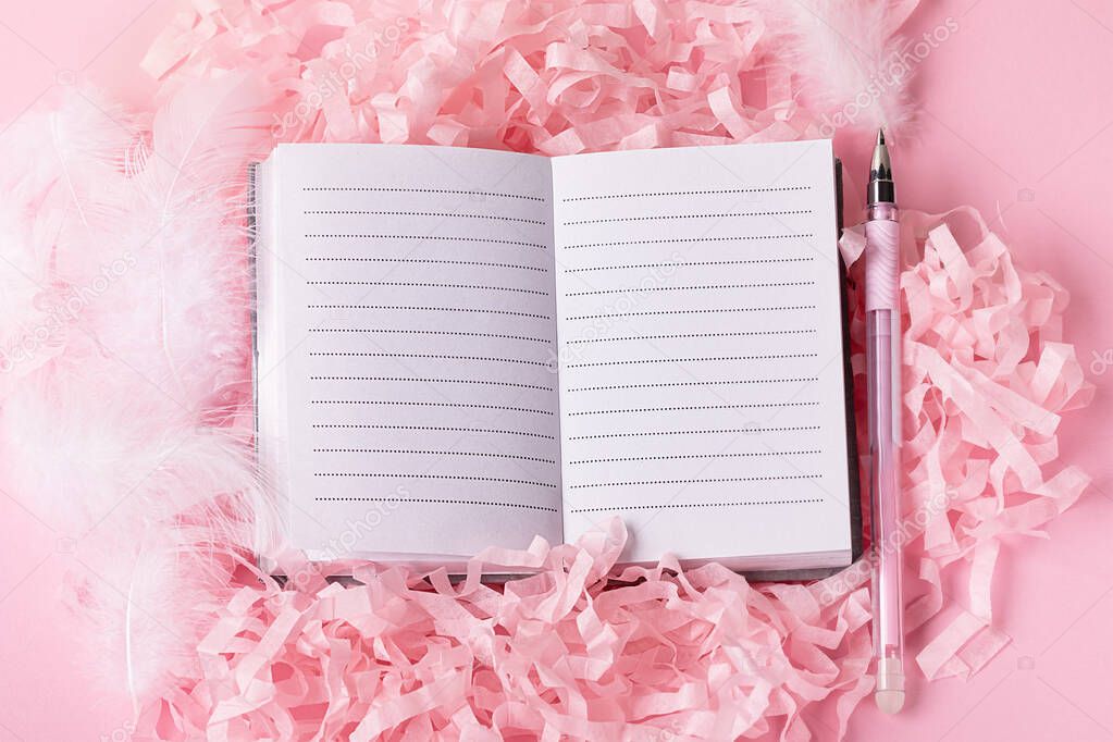 cute pink fluffy background with open notepad and  pen on decorative paper next to it. Top view of on girly stationery and white decorative feathers with ribbons