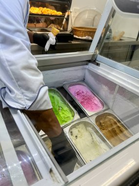 Tepsilerdeki dondurmaya ve camın arkasındaki satıcıya odaklan. Farklı renkte ve aromalı dondurma.