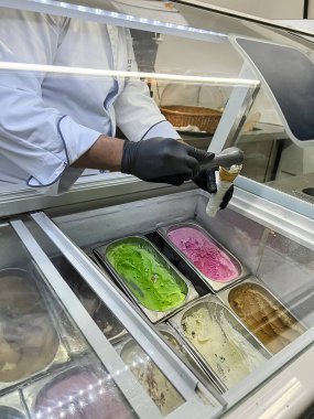 Tepsilerdeki dondurmaya ve camın arkasındaki satıcıya odaklan. Farklı renkte ve aromalı dondurma.