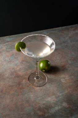 Tuzlu çerçeveli limonlu limonlu otantik margarita kokteyli, toprak renkli yüzey ve zarif koyu arkaplan, tekila, limon, acı portakal likörü ile süslenmiş lezzetli Meksika içeceği.