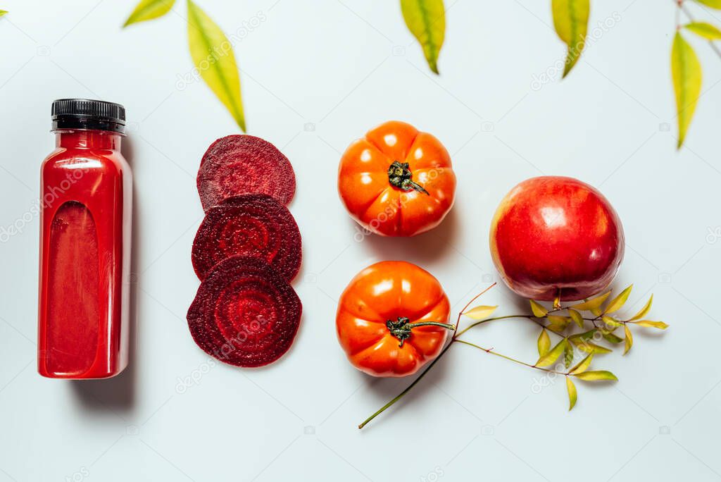 Red smoothie drink in bottle near ripe apples tomatoes and beets. Detox diet for healthy body and mind. health food concept. On light background