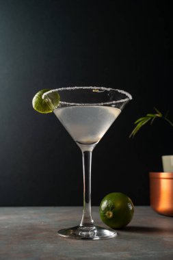 Tuzlu çerçeveli limonlu limonlu otantik margarita kokteyli, toprak renkli yüzey ve zarif koyu arkaplan, tekila, limon, acı portakal likörü ile süslenmiş lezzetli Meksika içeceği.