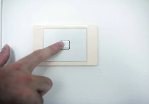 Finger switching off a wall mounted electrical light switch on a white interior house wall, close up view of the hand