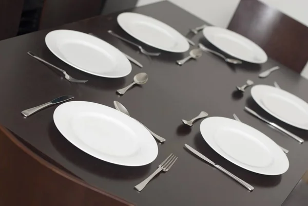 Black dining table set with clean white plates and cutlery for six in a tilted angle view