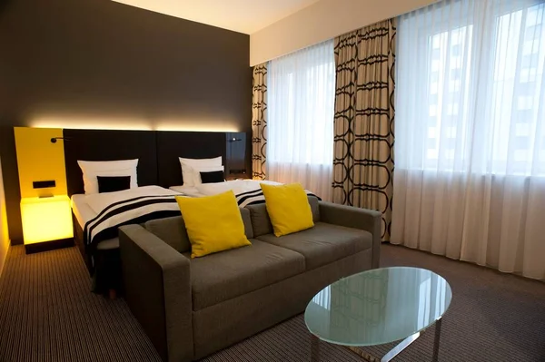 Modern empty bedroom suite with a double bed, couch and table and illuminated bedside table with neutral decor and yellow highlights