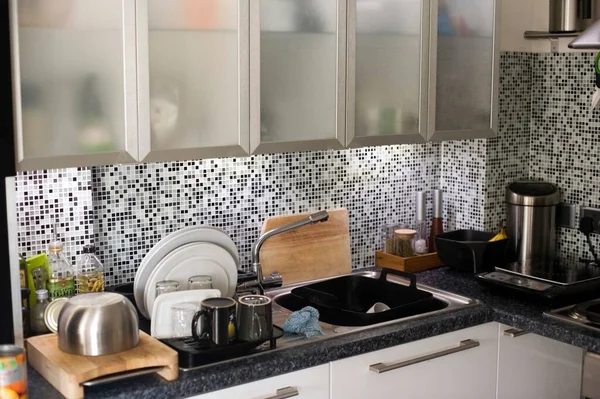 Modern kitchen with a tiled mosaic splashback, glass fronted cupboards and under cupboard lighting above the sink, filled with small appliances on the countertops