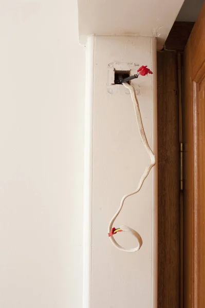 Mains wiring for a domestic electricity supply with conduit alongside a door in a DIY and renovation concept entering on open access point in the wall