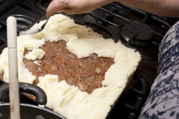 Cooking cottage pie adding the mashed potato topping or crust to the savory mince meat
